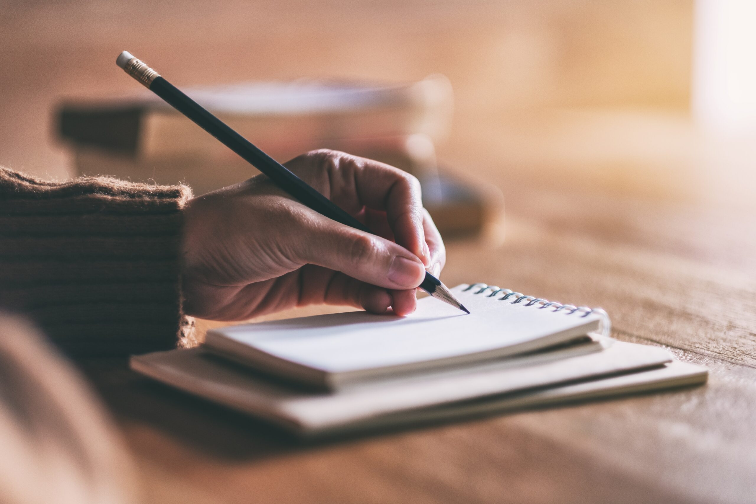 Closeup image of a woman writing on blank notebook on wooden table